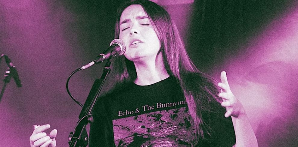 An image of a woman with long dark hair singing into a microphone.
