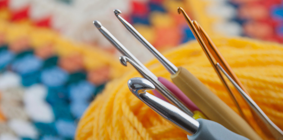 An image of crochet needles and yarn/wool in the background.