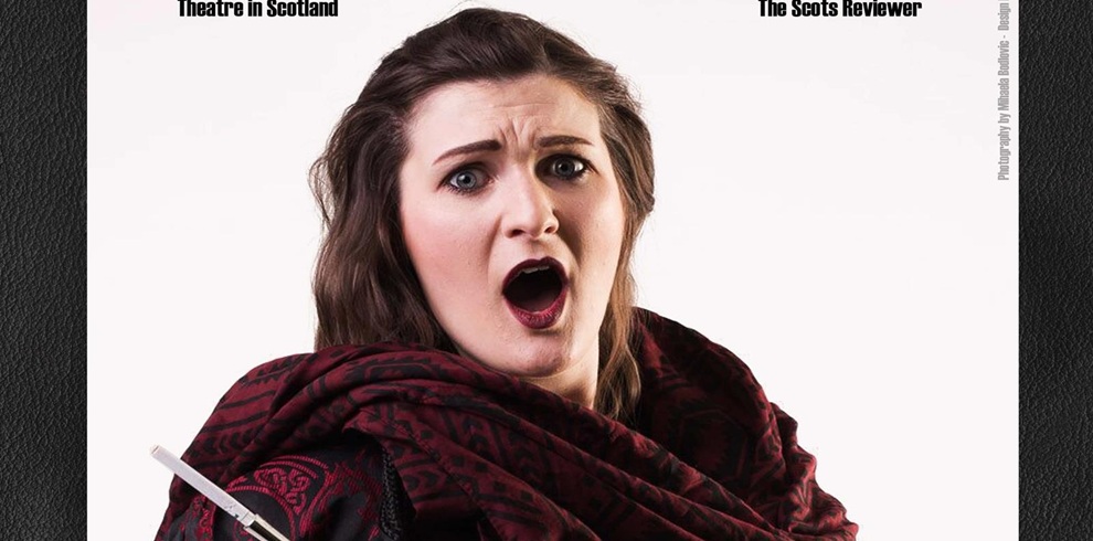 A woman with long brown hair, wearing a dark red and black patterned shawl, stands against a plain white background. She has a surprised or dramatic expression, her mouth open as if in mid-speech or song. The image appears to be part of a theatrical or promotional photo, with text at the top mentioning theatre in Scotland.