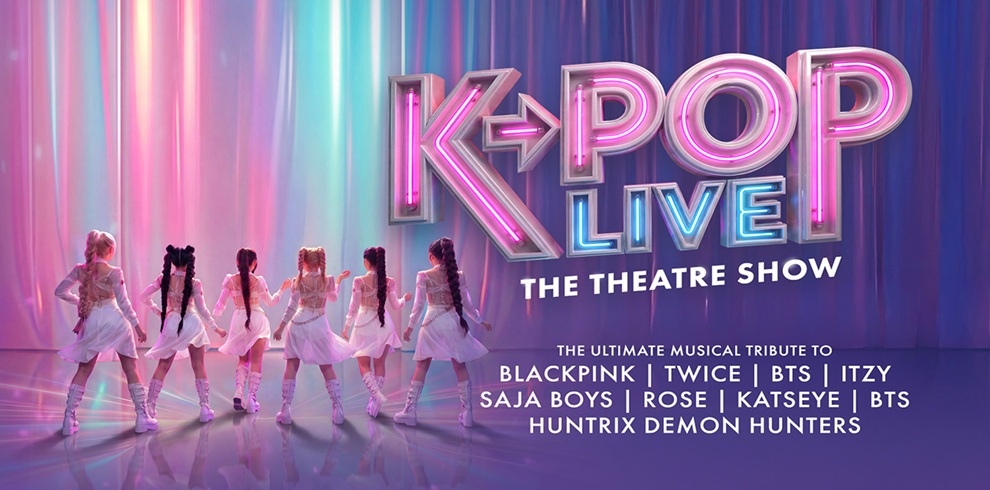 A promotional poster for “K‑POP LIVE: The Theatre Show.” The image shows a group of eight performers standing on a brightly lit stage with their backs facing the viewer. They wear coordinated shiny white outfits and knee‑high boots, illuminated by pink, purple, and blue lighting. Large neon‑style text on the right reads “K‑POP LIVE” with “THE THEATRE SHOW” underneath. Below, additional text states “The Ultimate Musical Tribute To BLACKPINK | TWICE | BTS | ITZY | SAJA BOYS | ROSE | KATSEYE | BTS | HUNTRIX DEMON HUNTERS.” Vertical pastel light streaks fill the background, giving the scene a futuristic concert atmosphere.
