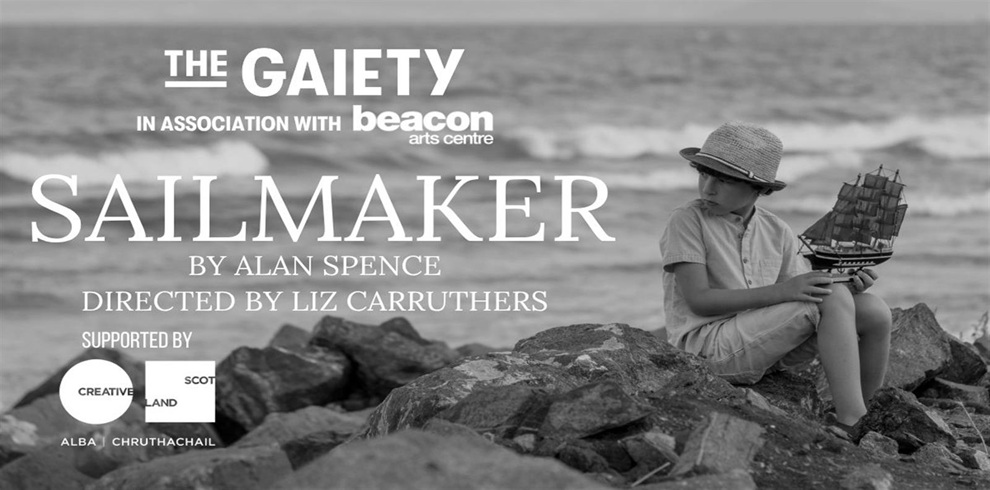 Black-and-white promotional poster for the play Sailmaker by Alan Spence, directed by Liz Carruthers. The text includes “The Gaiety in association with Beacon Arts Centre” and notes support from Creative Scotland. The background shows a young boy sitting on rocks by the sea, wearing a straw hat and light-colored clothes, holding a model sailing ship while looking down at it thoughtfully.