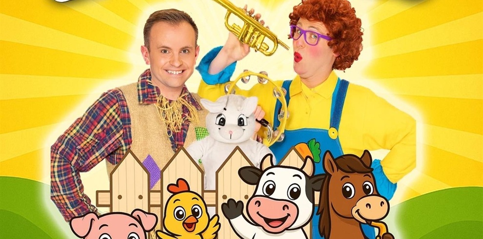 Bright, colorful promotional image featuring two performers dressed in cheerful farm-themed costumes. One person wears a plaid shirt and straw vest holding a white puppet goat, while the other wears a yellow shirt, blue overalls, and curly red wig, playing a toy trumpet. In front of them is a cartoon-style wooden fence with smiling animated farm animals—a pig, chick, cow, and horse—set against a sunny yellow background with rays and green hills.