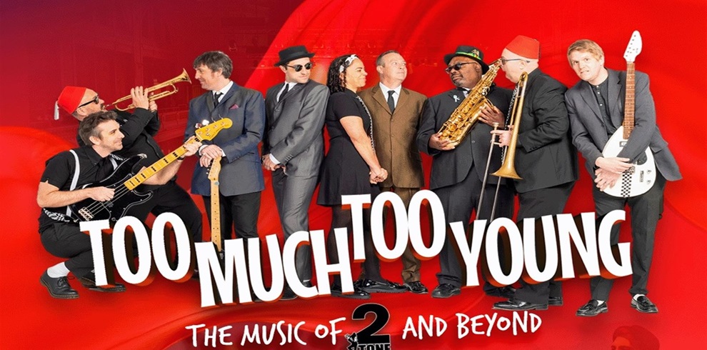 A group of musicians standing in a row against a bright red background, holding various instruments including a trumpet, saxophone, electric guitar, and bass guitar. They are dressed in suits and hats, with some wearing red fez-style hats. Large white text across the image reads “TOO MUCH TOO YOUNG,” and smaller text below says “The music of 2 Tone and beyond.