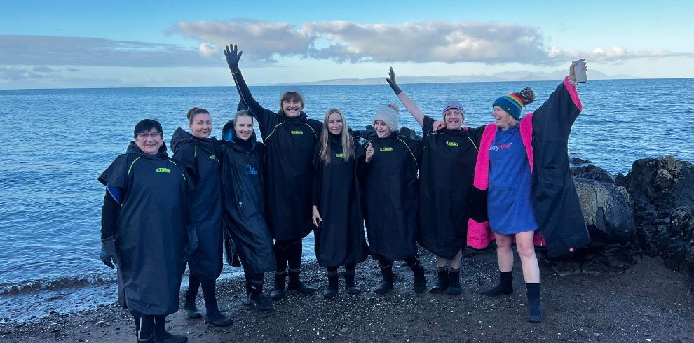 Several women standing on a beach posing for the camera after a wild swimming session.