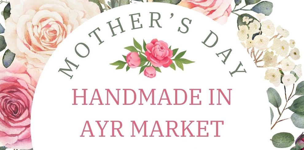 Decorative floral graphic advertising a Mother’s Day market, featuring soft pink and cream flowers around a circular design with the text “Mother’s Day – Handmade in Ayr Market” in elegant lettering.