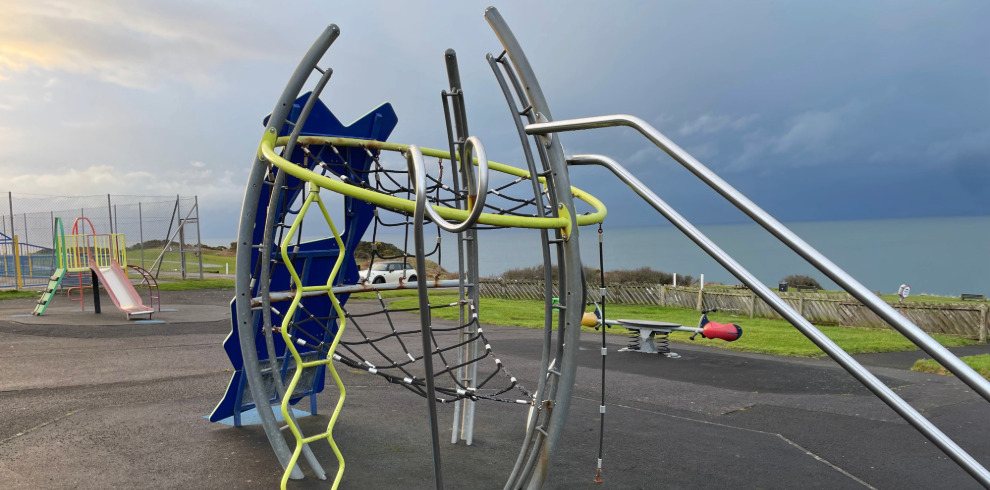 Outdoor play equipment at play park with coastal views.