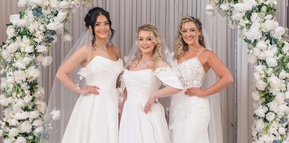 Three brides standing under a flower filled arch.