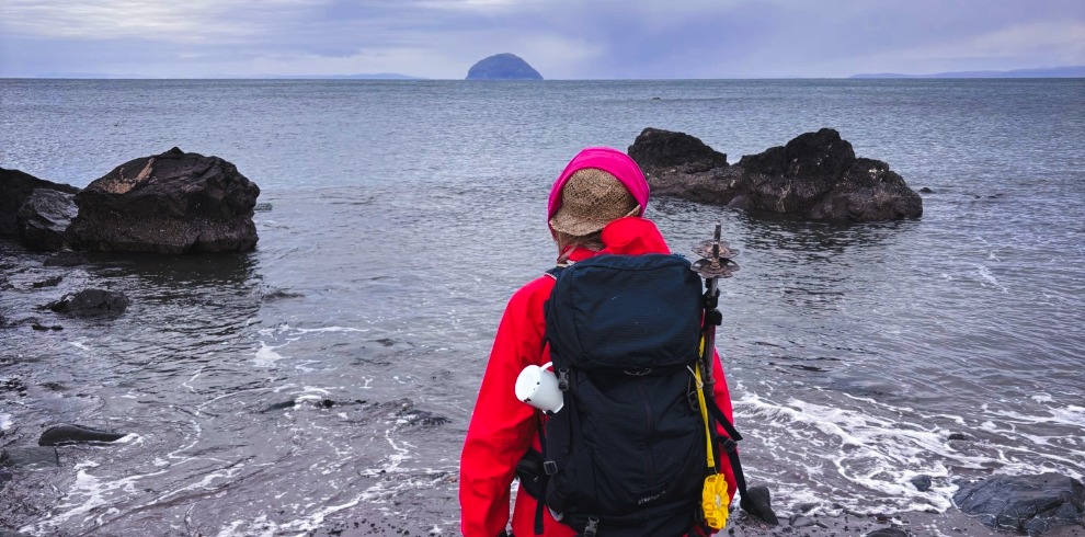 Woman in red with back pack walking on a beach.