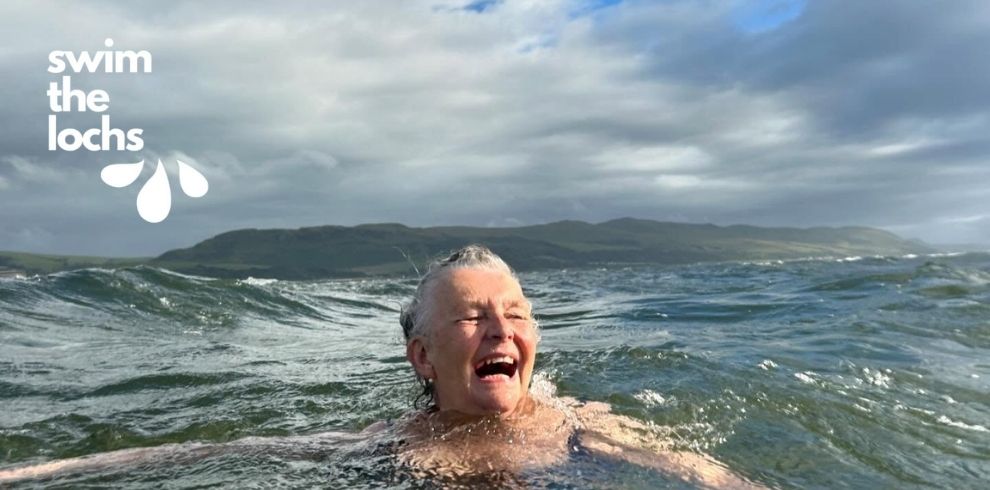 A person is swimming in open water with only the head and upper shoulders visible above the surface. The water around them is choppy with small rolling waves. In the distance, a long stretch of hilly shoreline is visible beneath a cloudy sky. In the top-left corner, the text “swim the lochs” appears alongside a small graphic of three water droplets.