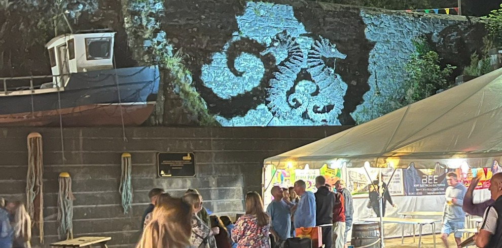 Two seahorse figures lit up on a wall. Food tent and small group of people.
