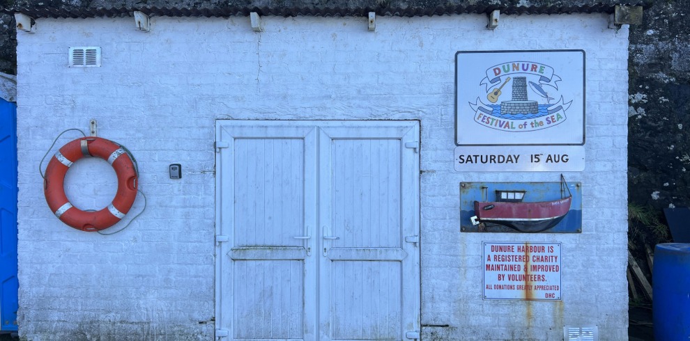 Wall of a boathouse with a sign for Dunure Festival of the Sea.