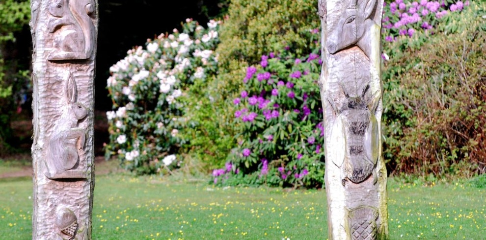 Carved poles with woodland creatures, spring flowers in bloom.