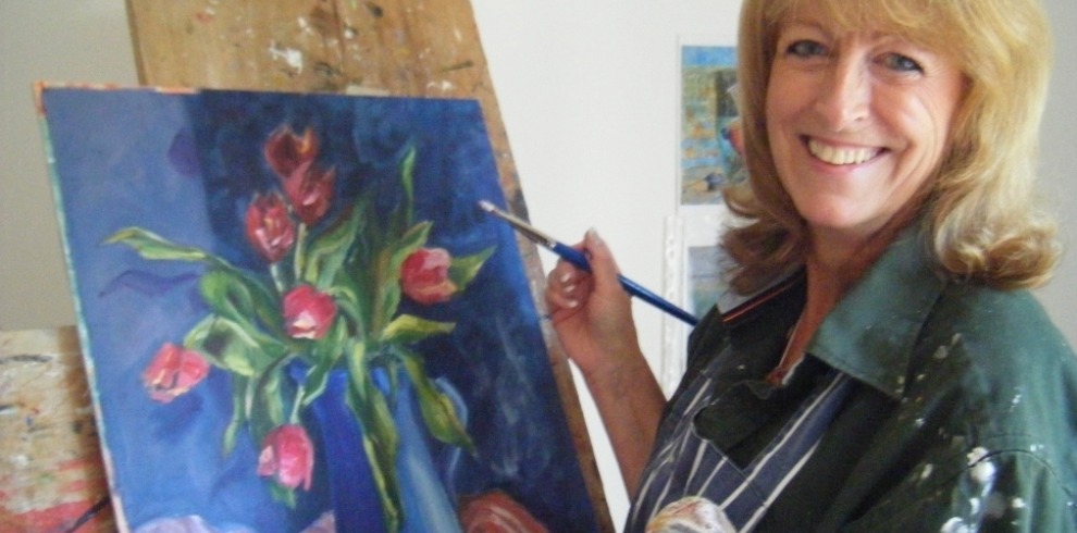 West Coast Canvas Exhibition and Workshops 8 Artist holding a paintbrush next to a painting on an easel.