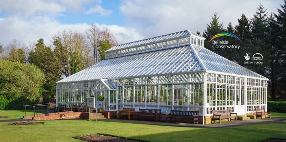 Promotional image for the Belleisle Conservatory. The image features an illustrated glass conservatory building surrounded by trees and landscaped gardens with flowerbeds in the foreground. The Belleisle Conservatory logo and Lottery Funded logos are present.