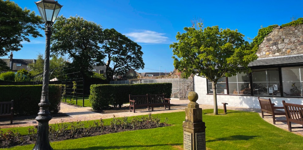 Garden on a sunny day with trees and box hedge. Stone monument feature.