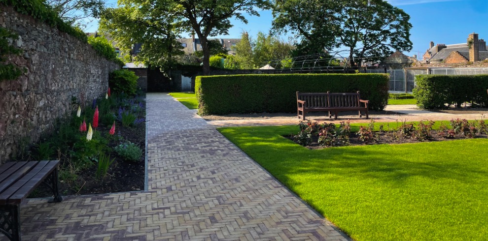 Stone pathway lined with flower beds. Box hedging and grass area.