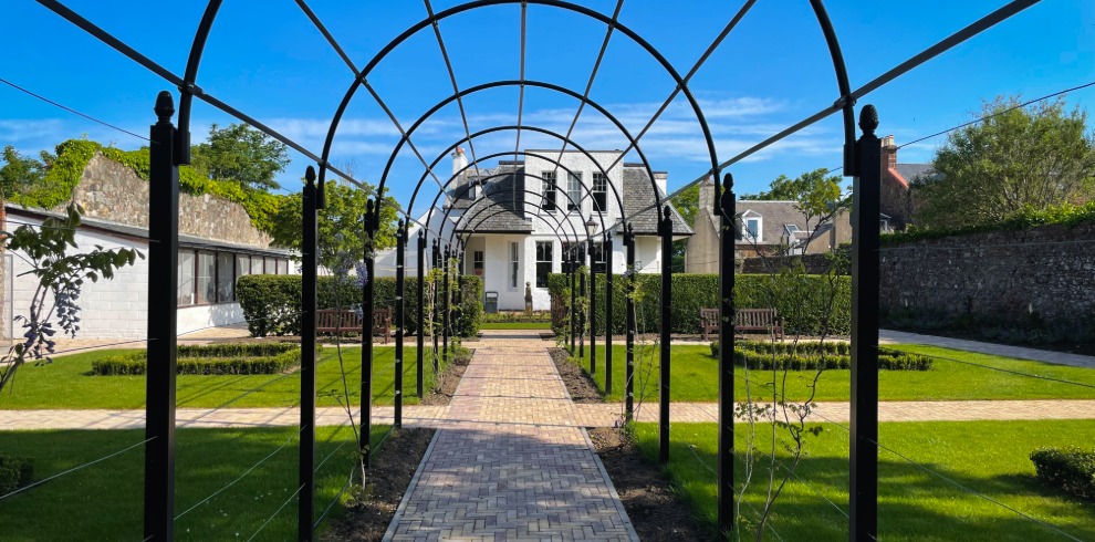 Trellis covered stone pathway leading to a white building.
