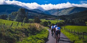 Cyclists on a narrow country round with view of hills in the distance.