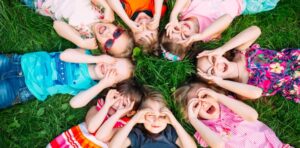 Children lying on some grass making funny faces.
