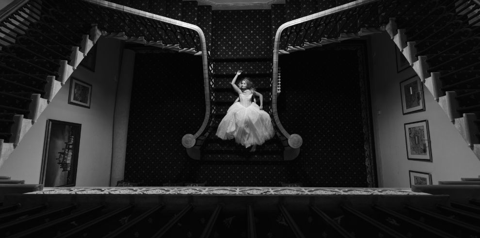 A black and white photo of a bride posing at the bottom of a staircase.