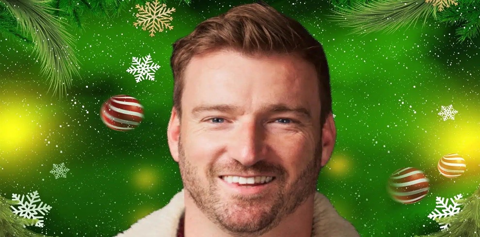 Close-up promotional image of a person smiling, shown from the shoulders up against a festive green background. The background is decorated with Christmas-themed elements including snowflakes, pine branches, and red-and-gold striped baubles. Soft glowing light effects add warmth to the scene. The person is wearing a jacket with a light-colored, shearling-style collar. The overall design has a cheerful holiday theme with bright green tones and seasonal decorations.