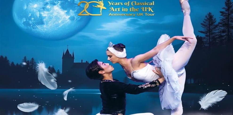 Promotional poster for a ballet production featuring two ballet dancers performing a lift. The dancer in a black outfit supports the dancer in a white classical tutu, who is balanced horizontally with one leg extended upward and arms outstretched in a graceful pose. The scene is set against a nighttime background with a large glowing moon, a lake reflecting the sky, and the silhouette of a castle and trees in the distance. White feathers float across the foreground, reinforcing a swan theme. At the top of the image, text reads “20 Years of Classical Art in the UK – Anniversary UK Tour,” with a stylized number 20 and a ballet figure incorporated into the design. The overall color palette features cool blue tones with soft lighting, creating a serene, theatrical atmosphere.