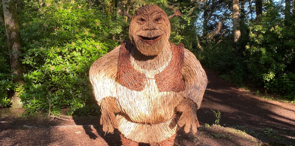 Willow sculpture of the character Shrek in an park setting.
