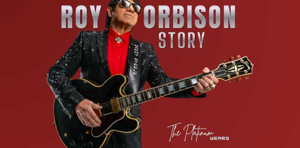 Promotional image on a dark red background featuring a performer holding a black electric guitar and wearing dark sunglasses, a red shirt, and a black sequined jacket. Large silver text across the top reads “ROY ORBISON STORY.” In the lower right corner, white script text reads “The Platinum Years.”
