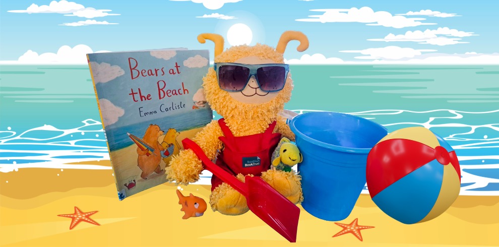 Bookbug in the Park 5 A plush yellow toy wearing oversized sunglasses and a red outfit sits on a cartoon-style beach scene. Beside the toy is a children's book titled Bears at the Beach by Emma Carlisle. A red plastic shovel lies in front, with a blue bucket and a colorful beach ball to the right. Small toy sea creatures, including a fish and a starfish, are scattered on the sand. The background shows a calm blue sea, white clouds, and a bright sun in the sky.