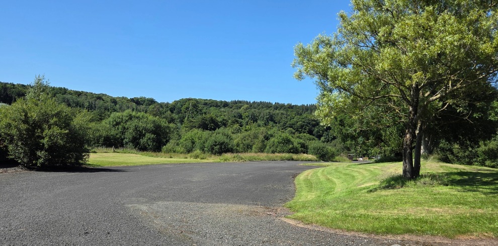 Concrete road, surrounded by grass with view of green hills in the background.