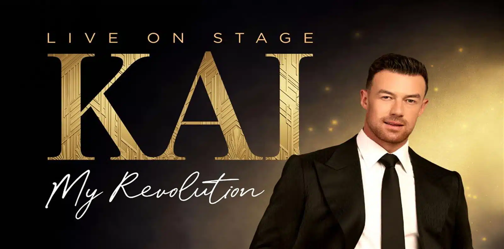 Promotional poster for the live stage production KAI: My Revolution. The design features large gold lettering spelling “KAI” on a dark black and gold background with subtle glowing light effects. A person wearing a black suit, white shirt, and black tie stands on the right side of the image. Visible text reads: “LIVE ON STAGE,” “KAI,” and “My Revolution.”