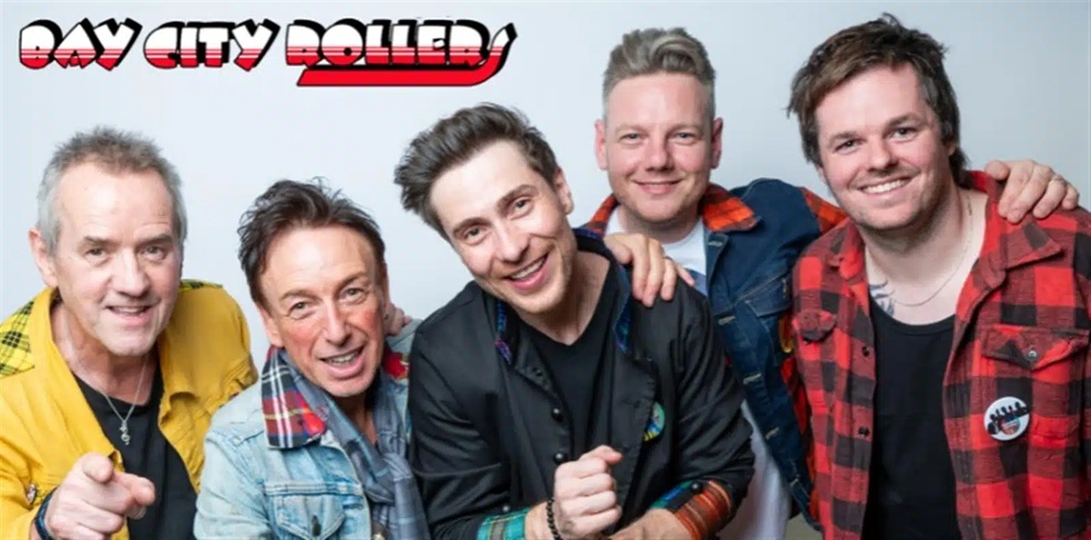 Promotional photo of the Bay City Rollers featuring five band members posing together against a light grey background. The group is dressed in casual clothing including tartan-patterned shirts and denim jackets. The Bay City Rollers logo appears in the top left corner in red, white and black. The band members are positioned closely together facing the camera in a studio-style image.