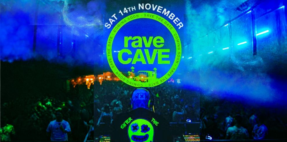 Promotional image for a rave event in a dark indoor venue filled with blue and green lighting and haze. A DJ wearing headphones stands at a mixing desk in the foreground facing a crowd. At the top center, a large circular graphic displays the text “SAT 14TH NOVEMBER” and “rave CAVE,” with “SAVE THE DATE” and “COMING SOON” repeated around the border. Neon lights and fog create an energetic nightclub atmosphere.