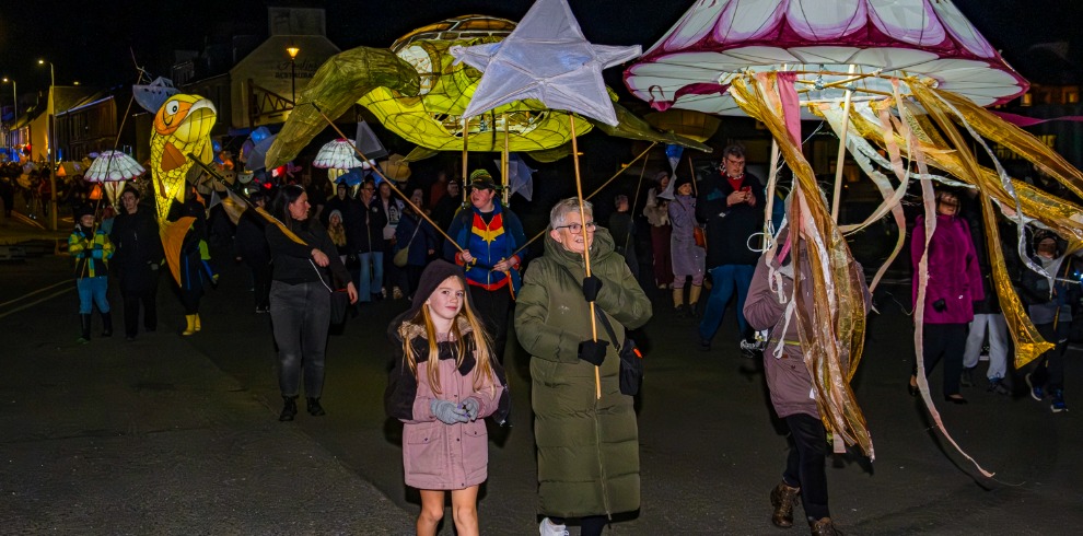 Nightime parade. Families holding lit lanterns.