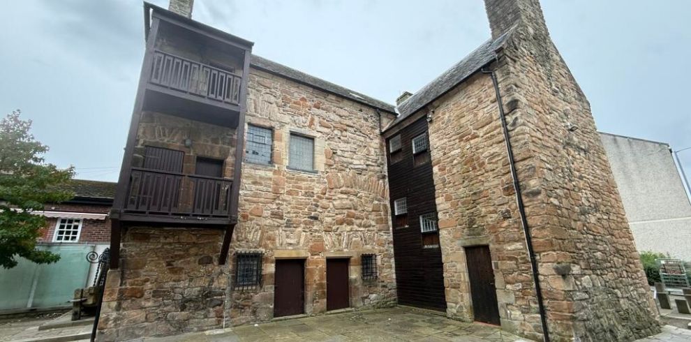 Exterior view of Loudoun Hall, a historic stone townhouse in Ayr. The medieval building features traditional stone masonry, small leaded windows, timber external balconies and a prominent stone tower. The courtyard setting highlights the building's historic architecture and heritage character, showcasing one of Scotland's oldest surviving townhouses and event venues.