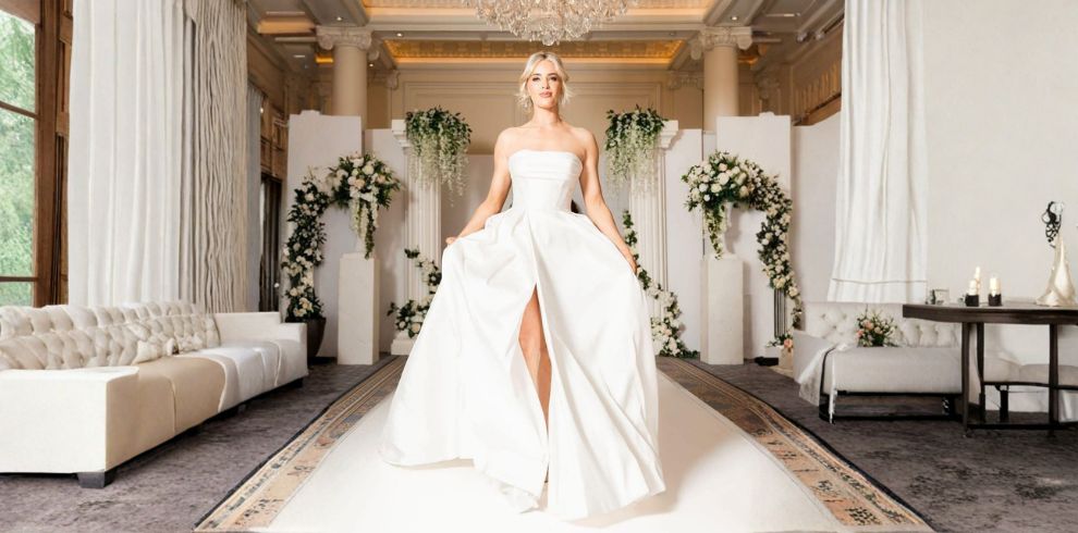 The image shows bridal catwalk scenes at an elegant wedding exhibition venue, featuring wedding dresses on a runway surrounded by floral displays, chandeliers and seated visitors watching the fashion showcase. The setting highlights wedding inspiration, bridal fashion and wedding planning services available at the event.