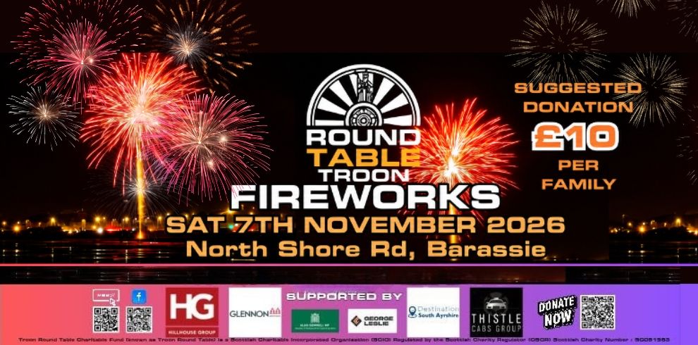Promotional banner for the Troon Round Table Fireworks event. Multiple red, pink and gold fireworks explode over a dark waterfront at night, with reflections visible on the water. The centre of the image features the Round Table Troon logo above the event title: “Fireworks”, followed by the date “Saturday 7th November 2026” and location “North Shore Rd, Barassie”. On the right-hand side, text states “Suggested Donation £10 Per Family”. Along the bottom is a row of sponsor logos, QR codes and donation information displayed on a purple and red banner. The overall design uses bright fireworks against a black night sky to promote the community fireworks display.