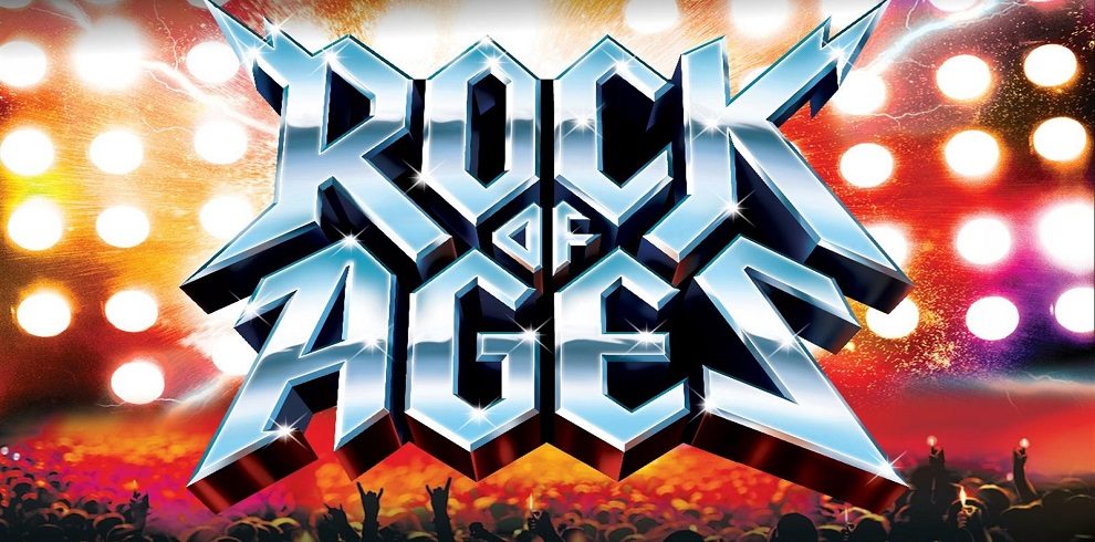 A promorional advert for Rock of Ages. The font Rock of Ages is in silver font against a rock theme background with bright lights and people standing in front of the stage with their arms up in the air, having a good time.