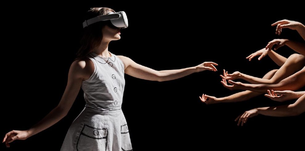 A lady with a VR set on reacshing out to hands that can be seen on the right of the image.
