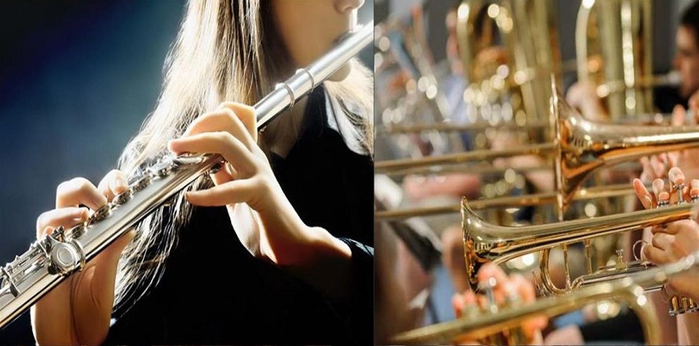 A split-screen image featuring musicians playing different wind instruments. On the left side, a close-up of a person playing a silver flute, with fingers pressing the keys and a soft light illuminating the scene. On the right side, a group of musicians playing brass instruments, primarily trumpets, with a blurred background of additional brass players in a concert or band setting.