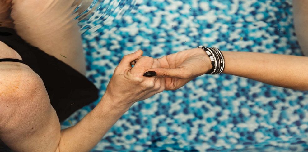 two people holding hands over a pool of water.